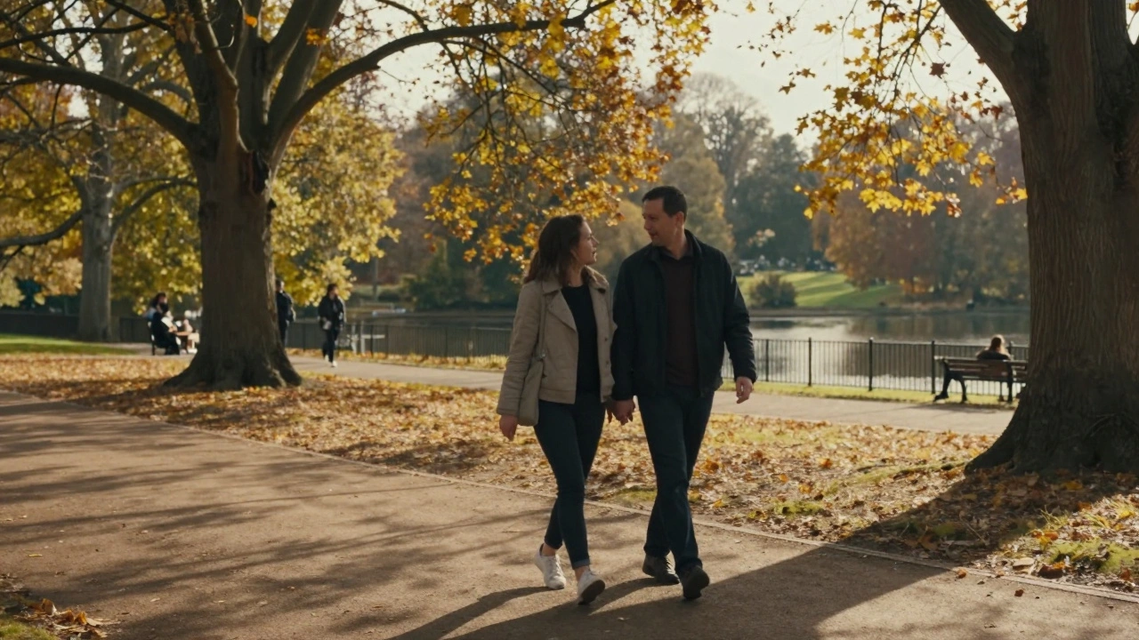 Two people walking hand in hand through Hyde Park at sunset, autumn leaves falling around them.