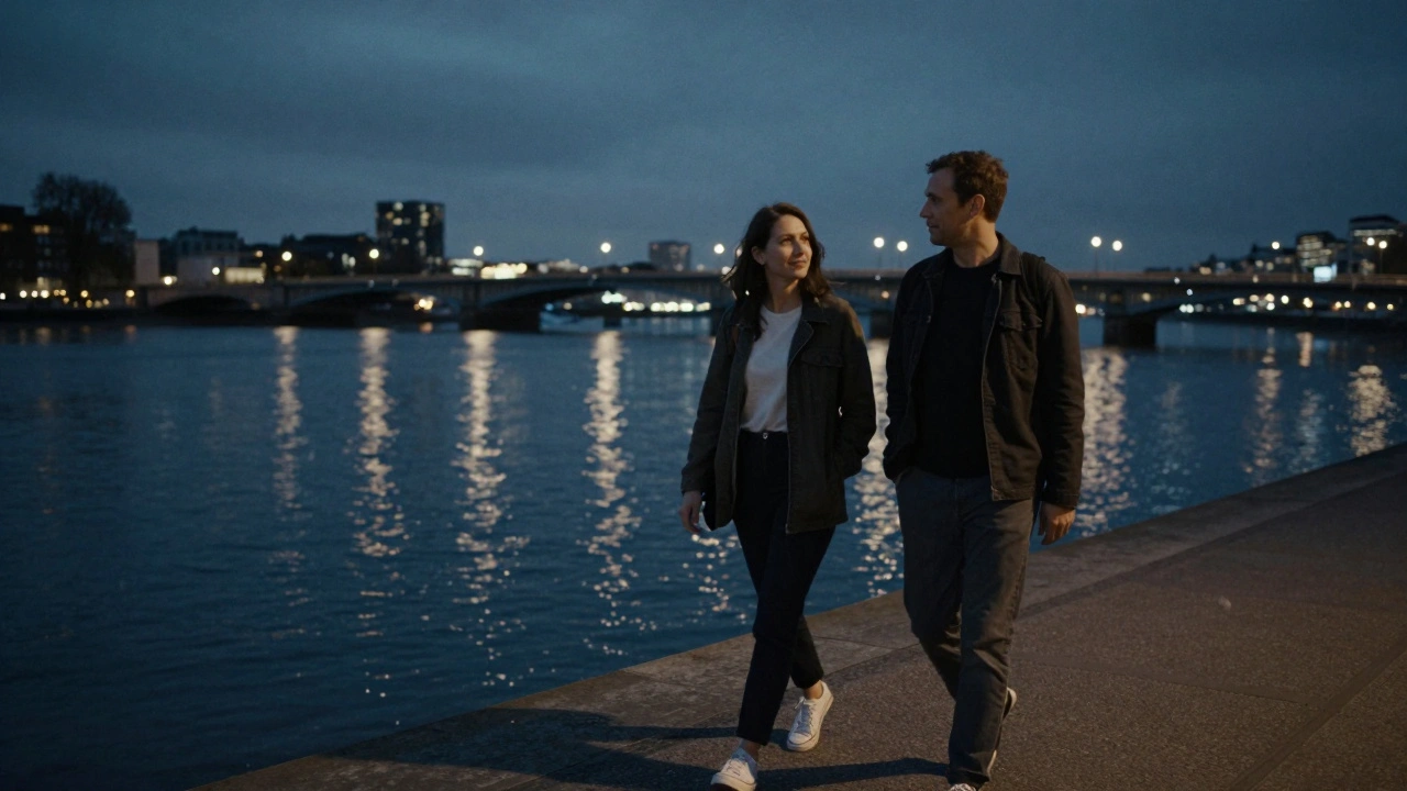 Two people walking peacefully along the Thames at night, illuminated by city lights and water reflections.